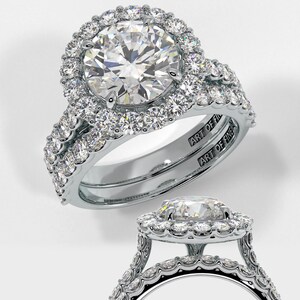 May include: A silver engagement ring set with a large round centre stone surrounded by a halo of smaller stones. The band is also set with smaller stones. The ring is engraved with the words "Art of Fine Jewellery".