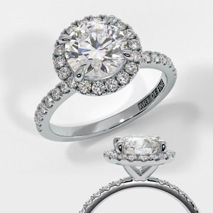 May include: A silver engagement ring featuring a round centre diamond encircled by a halo of smaller diamonds. The band is also set with smaller diamonds. The ring is engraved with the words "Art of Fine".
