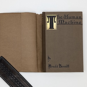 May include: A brown hardback book with a gold-lettered title "The Human Machine" by Arnold Bennett.