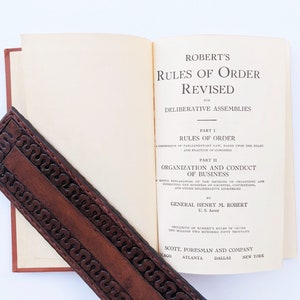 May include: A vintage, cream-colored book titled "Robert's Rules of Order Revised" for deliberative assemblies. The book is open to the title page and the author is listed as General Henry M. Robert, U.S. Army. The book is published by Scott, Foresman and Company.