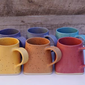 Pode incluir: Seis canecas de cer&acirc;mica em v&aacute;rias cores, incluindo amarelo, laranja, vermelho, azul e roxo. As canecas t&ecirc;m um esmalte salpicado e uma forma quadrada com cantos arredondados.