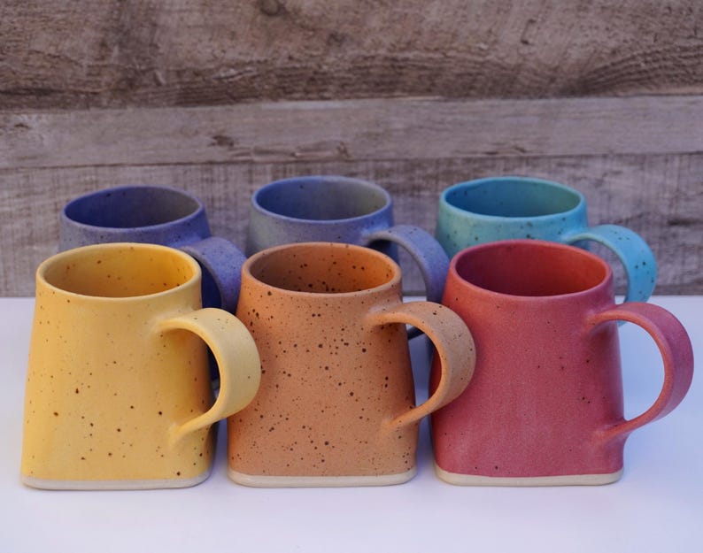 Pode incluir: Seis canecas de cer&acirc;mica em v&aacute;rias cores, incluindo amarelo, laranja, vermelho, azul e roxo. As canecas t&ecirc;m um esmalte salpicado e uma forma quadrada com cantos arredondados.