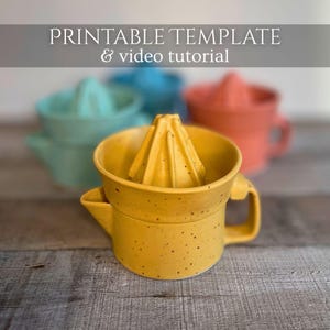 May include: A yellow ceramic citrus juicer with a speckled finish, a central reamer, and a side handle. The text PRINTABLE TEMPLATE & video tutorial is visible at the top. Out-of-focus teal and coral juicers are positioned in the background.