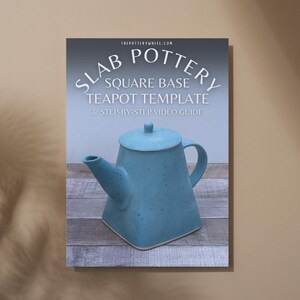 May include: A blue square-based teapot with a matching lid is featured on a poster. The poster includes the text "SLAB POTTERY SQUARE BASE TEAPOT TEMPLATE & STEP-BY-STEP VIDEO GUIDE" and the website address "THEPOTTERYWHEEL.COM". The teapot is displayed on a wooden surface.