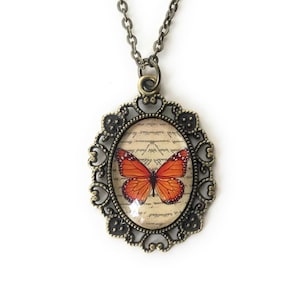 Monarch butterfly necklace. Oval shaped pendant with a filigree edging. Image is set under a glass cabochon. Pendant measures 1 inch x 1.5 inches