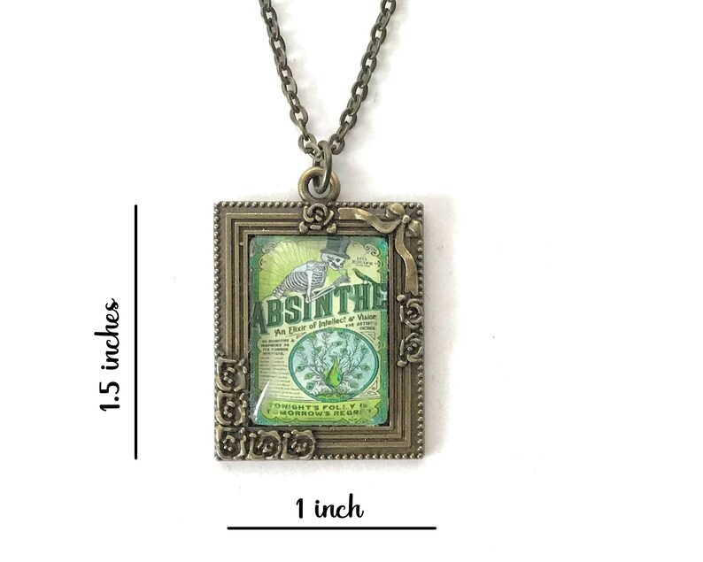 May include: A bronze pendant necklace with a square frame featuring a vintage-style illustration of a skeleton holding a bottle of absinthe. The illustration is surrounded by a decorative floral border. The pendant measures 1 inch by 1.5 inches.