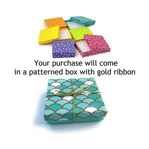 May include: A teal gift box with a white and teal scale pattern. The box is tied with a gold ribbon.  "Your purchase will come in a patterned box with gold ribbon."