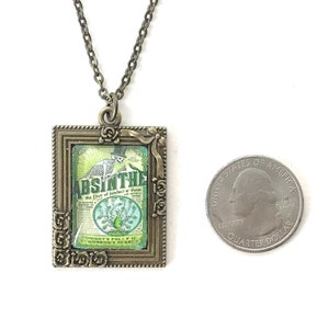 May include: A bronze pendant necklace with a framed image of a vintage absinthe bottle label. The label features a skeleton holding a glass of absinthe and the text "Absinthe, An Elixir of Indolence & Vision".