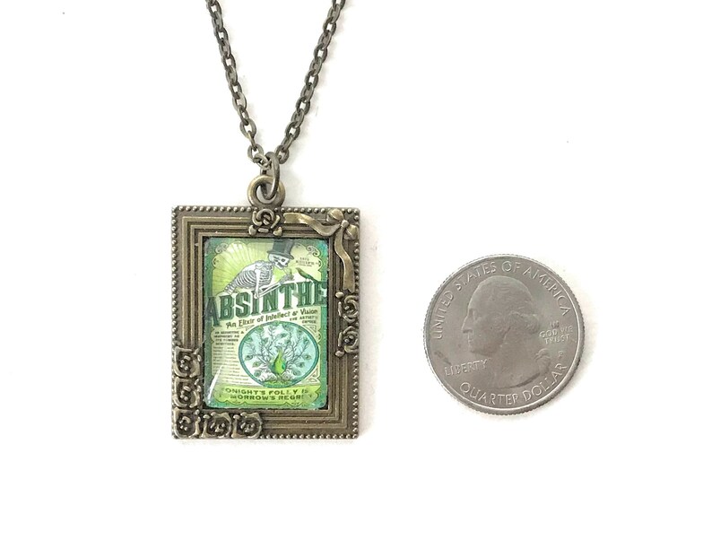 May include: A bronze pendant necklace with a framed image of a vintage absinthe bottle label. The label features a skeleton holding a glass of absinthe and the text "Absinthe, An Elixir of Indolence & Vision".