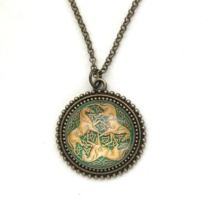 Celtic horse necklace.  3 golden colored horses intertwined with Celtic knots on a green background. Image is placed under a glass cabochon and placed into a brass tray setting with a beaded edge. Chain is 24 inches long.