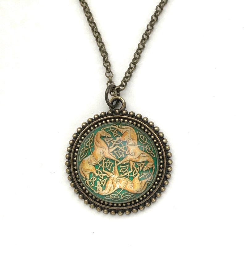 Celtic horse necklace.  3 golden colored horses intertwined with Celtic knots on a green background. Image is placed under a glass cabochon and placed into a brass tray setting with a beaded edge. Chain is 24 inches long.