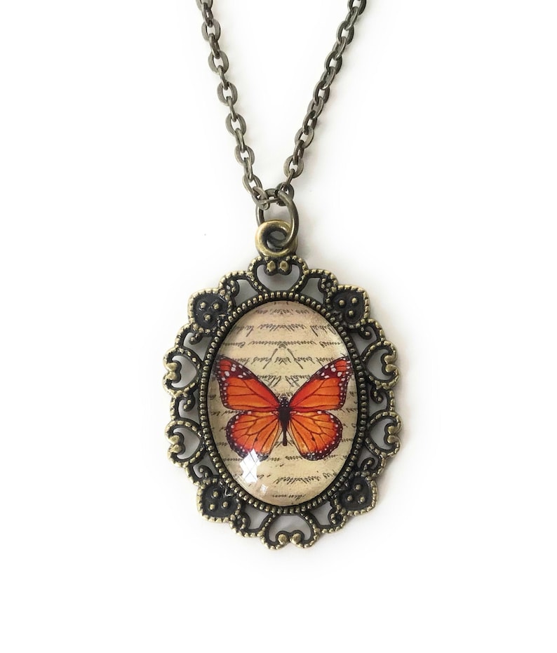Monarch butterfly necklace. Oval shaped pendant with a filigree edging. Image is set under a glass cabochon. Pendant measures 1 inch x 1.5 inches