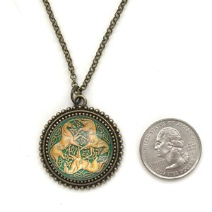 Celtic horse necklace.  3 golden colored horses intertwined with Celtic knots on a green background. Image is placed under a glass cabochon and placed into a brass tray setting with a beaded edge. Chain is 24 inches long.