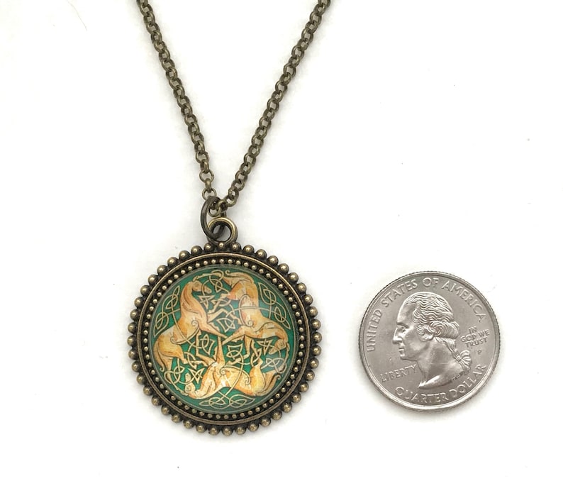 Celtic horse necklace.  3 golden colored horses intertwined with Celtic knots on a green background. Image is placed under a glass cabochon and placed into a brass tray setting with a beaded edge. Chain is 24 inches long.