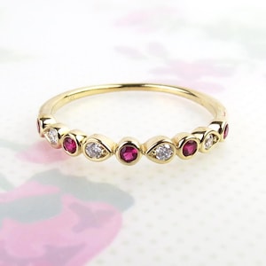 Peut inclure: Une fine bague en or avec un motif alterné de rubis ronds sertis clos et de diamants blancs transparents. L'anneau en métal porte le poinçon 14K, indiquant la pureté de l'or. Les pierres sont disposées en une rangée continue sur le devant.