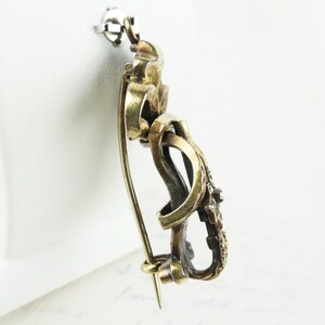 May include: Vintage gold-toned brooch with intricate looping design and small, embedded gemstones. The pin features a classic clasp and a decorative, ornate style, suitable for formal wear or adding a touch of elegance.
