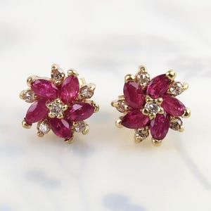 May include: A pair of gold stud earrings, each designed as a flower with six marquise-cut deep pink rubies forming the petals, accented by small round clear diamonds set between the petals and at the centre of each floral arrangement.