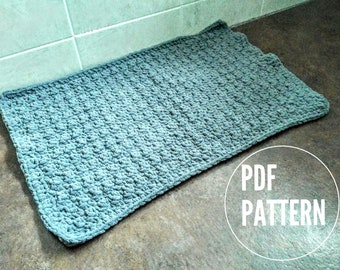 May include: A teal blue crocheted rug with a textured pattern. The rug is lying on a brown surface with the text "PDF PATTERN" in white.