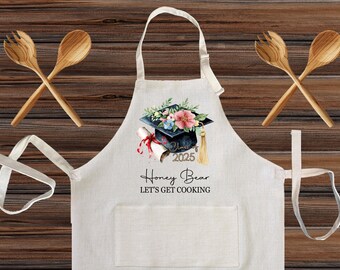 Può includere: Grembiule bianco sporco con tasca, con un design di cappello di laurea con fiori, un diploma e il testo "2025 Honey Bear LET'S GET COOKING." Include due cucchiai di legno.