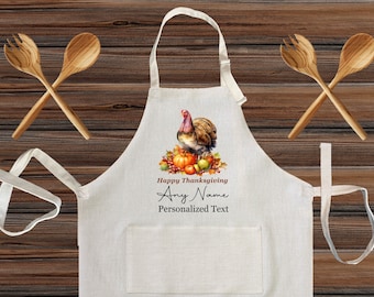 Può includere: Un grembiule bianco con un motivo di tacchino e raccolto autunnale, tra cui zucche e uva. Il grembiule ha il testo "Happy Thanksgiving" e spazio per testo personalizzato. Due cucchiai di legno per l'insalata sono incrociati sopra.