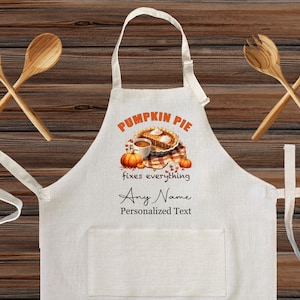 May include: White kitchen apron with a pumpkin pie, coffee cup, and pumpkins design. The text reads "Pumpkin Pie fixes everything" and "Any Name Personalized Text".