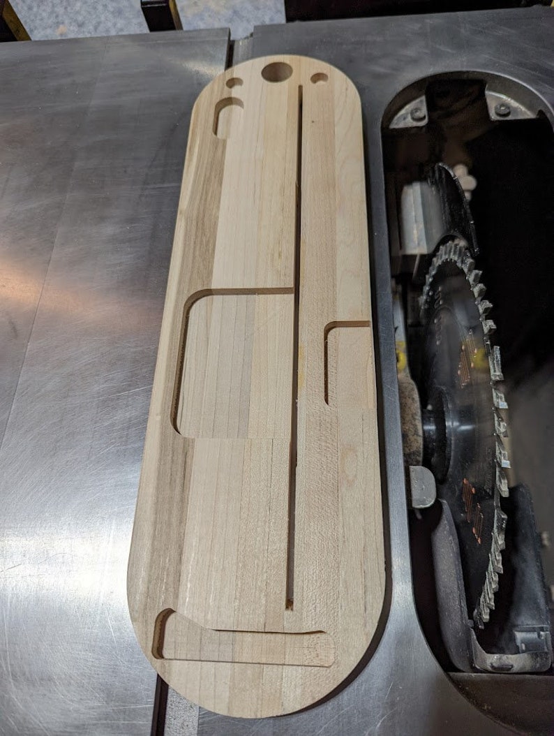 Puede incluir: Una tabla de madera con recortes para sujetar herramientas. La tabla es de color marr&oacute;n claro y tiene un acabado liso. Est&aacute; sentada en una sierra de mesa.