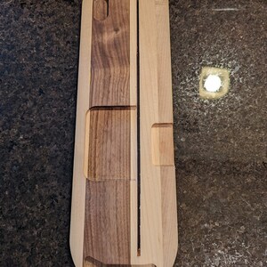 Puede incluir: Una bandeja de servir de madera con una ranura larga y estrecha en el centro y dos ranuras m&aacute;s peque&ntilde;as a cada lado. La bandeja est&aacute; hecha de dos tipos diferentes de madera, una clara y otra oscura.