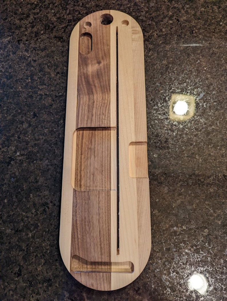 Puede incluir: Una bandeja de servir de madera con una ranura larga y estrecha en el centro y dos ranuras m&aacute;s peque&ntilde;as a cada lado. La bandeja est&aacute; hecha de dos tipos diferentes de madera, una clara y otra oscura.