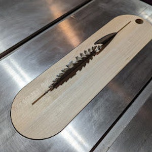 Może przedstawiać: Drewniana zakładka do książki z laserowo wyciętym wzorem sosny. Zakładka ma owalny kształt i ma otwór na górze na wstążkę.