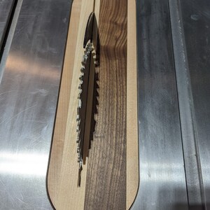 Puede incluir: Una tabla de cortar de madera con un recorte circular para una hoja de sierra. La tabla est&aacute; hecha de tres tipos diferentes de madera: arce, nogal y cerezo. La hoja de sierra es visible a trav&eacute;s del recorte.