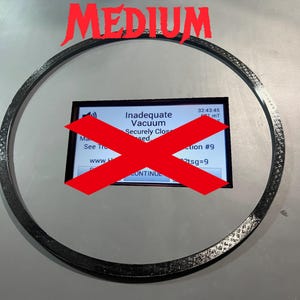 May include: A black ring with a textured surface. A red X is over a screen that reads "Inadequate Vacuum Securely Closed" and "Continue". The text "MEDIUM" is at the top of the image.