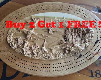 Puede incluir: Tablero de cribbage ovalado de madera con una escena natural tallada de patos, juncos y árboles. El tablero tiene agujeros para clavijas y el texto "Buy 2 Get 1 FREE!!!". Se ve una baraja de cartas.