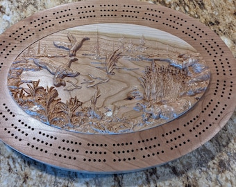 Puede incluir: Un tablero de cribbage de madera con una escena tallada de gansos volando sobre un estanque. El tablero tiene forma ovalada y tiene una mancha marrón.