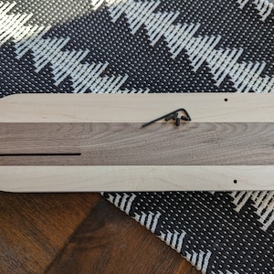 Puede incluir: Una bandeja de servir de madera con un borde de madera clara y un centro de madera oscura. La bandeja tiene un agujero redondo en un extremo y una ranura larga y estrecha en el centro. Hay tres peque&ntilde;os tornillos visibles en la parte superior de la bandeja.