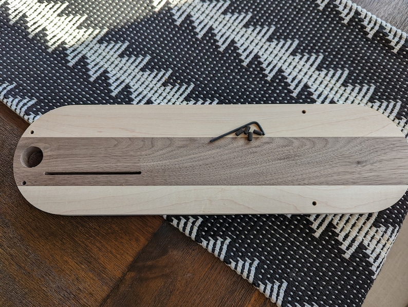 Puede incluir: Una bandeja de servir de madera con un borde de madera clara y un centro de madera oscura. La bandeja tiene un agujero redondo en un extremo y una ranura larga y estrecha en el centro. Hay tres peque&ntilde;os tornillos visibles en la parte superior de la bandeja.