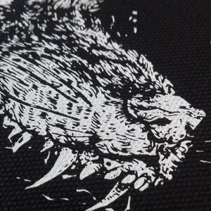 May include: A black and white graphic of a snarling wolf's head. The illustration features detailed fur and sharp teeth, set against a dark background. The design is bold and striking.
