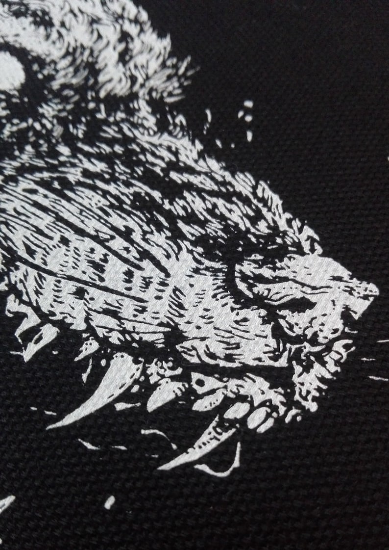 May include: A black and white graphic of a snarling wolf's head. The illustration features detailed fur and sharp teeth, set against a dark background. The design is bold and striking.