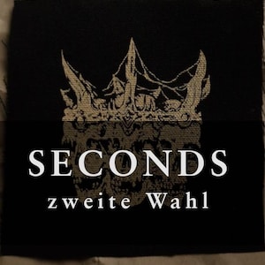 Könnte beinhalten: Schwarzer Stoffaufnäher mit einem goldfarbenen Kronenmuster und dem Wort "SECONDS" in Weiß. Der Text "zweite Wahl" ist ebenfalls in Weiß. Der Markenname "drowned orange" befindet sich unten.