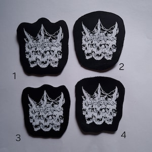 May include: Four black leather patches with a white design of three skulls wearing a crown with spikes. The patches are numbered 1 through 4.