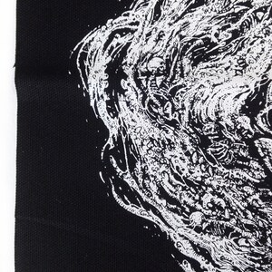 May include: Black fabric with a detailed white illustration. The artwork features a complex, swirling design with organic shapes and a textured appearance. The image is a close-up, highlighting the contrast between the black background and the intricate white design.