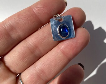 May include: A silver pendant with a blue oval gemstone set in a square frame.