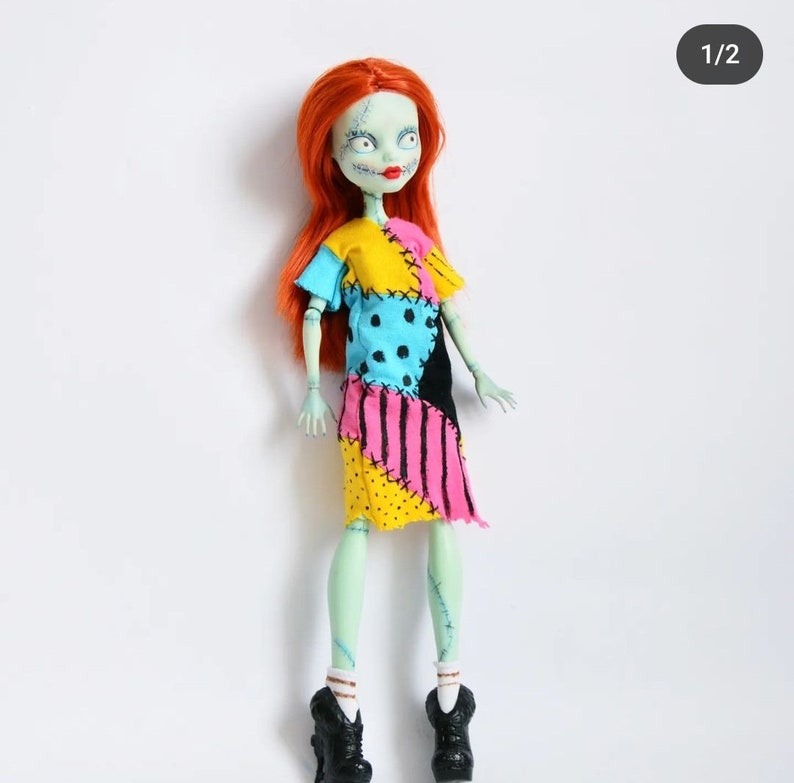K&ouml;nnte beinhalten: Eine Puppe mit gr&uuml;ner Haut und roten Haaren, die ein buntes Patchworkkleid und schwarze Schuhe tr&auml;gt. Die Puppe hat gen&auml;hte N&auml;hte auf ihrem Gesicht und K&ouml;rper.
