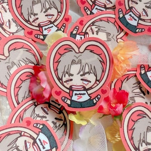 May include: A collection of stickers featuring a cartoon character with gray hair, framed by a pink heart. The character is wearing a white shirt with a red "7" and black shorts. Small red hearts are scattered around the heart-shaped frame.