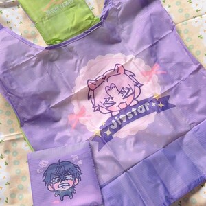 May include: A set of three reusable shopping bags in shades of purple and green. The large bag features a cartoon character design with the text "Jinstar". The smaller bags have cartoon character designs. The bags are folded and ready for use.