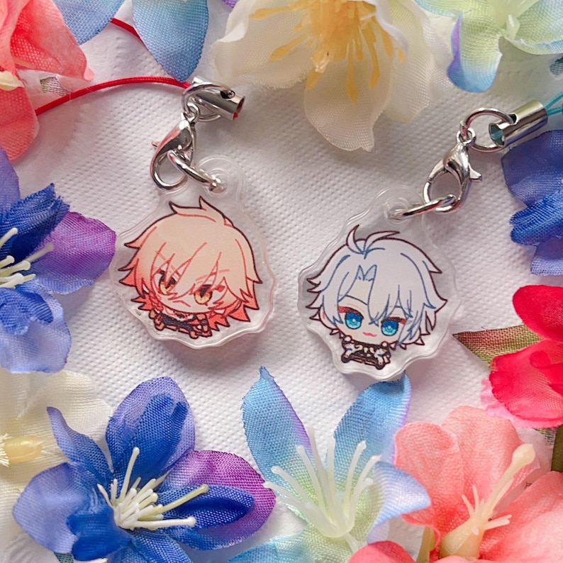 May include: Two anime-style character keychains. One keychain features a character with peach-colored hair and orange eyes, the other has white hair and blue eyes. Both are on silver-colored clasps, surrounded by colorful flowers.