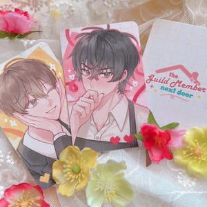 May include: Three illustrated cards with anime-style characters. One card has the text "the Guild Member next door". The cards are surrounded by pink and yellow flowers, set against a soft, blurred background.