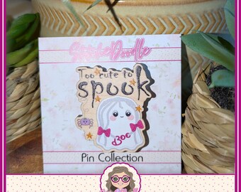 May include: A wooden pin featuring a ghost illustration with the text Too cute to spook, pink bows, and a small purple spider. The pin is mounted on a white backing card with the text StitchDoodle Pin Collection and a cartoon character logo.