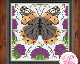 May include: A framed cross-stitch pattern featuring a central butterfly with gray, orange, and white wings, surrounded by purple thistle flowers and green stems on a white background. A circular logo with the text Stitch e Doodle is visible.