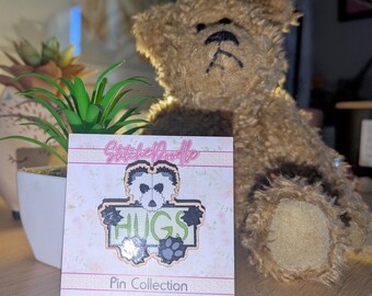 May include: A square display card featuring the text StitcheDoodle and Pin Collection, with a central pin design showing a stylized panda face above the word HUGS in green letters, accented by black paw prints and a light-colored background.