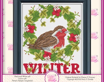 May include: A cross-stitch pattern featuring a brown and red robin centered within a circular wreath of green leaves, red flowers, and white blossoms. The word WINTER is printed in bold red capital letters at the bottom of the design.